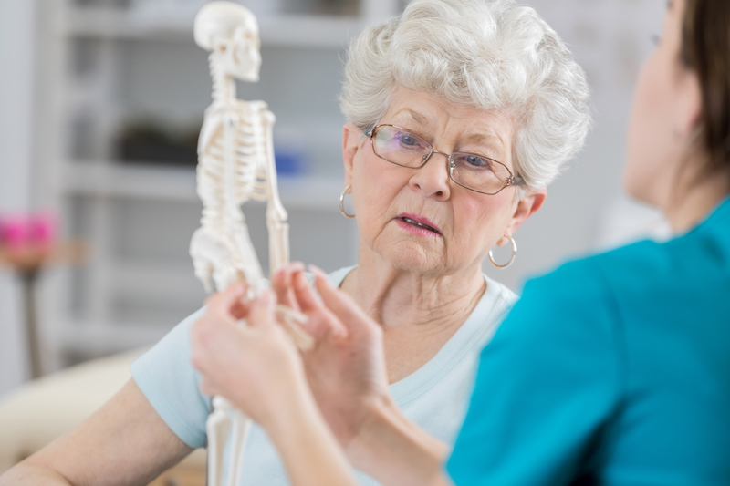 Health provider using toy skeleton to educate senior woman about aging bones