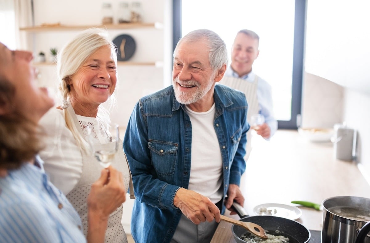 Group of senior friends at dinner party at home, cooking.