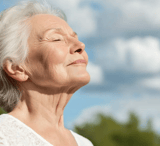 Elder woman facing the sunlight with a smile on her face
