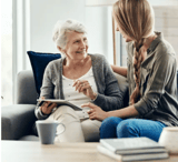 Elder woman smiling at younger woman while holding a tablet