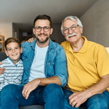 Three generations of a family sitting on a couch, smiling at the camera.