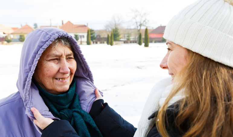 Young woman helping senior woman with coat on snowy day 
