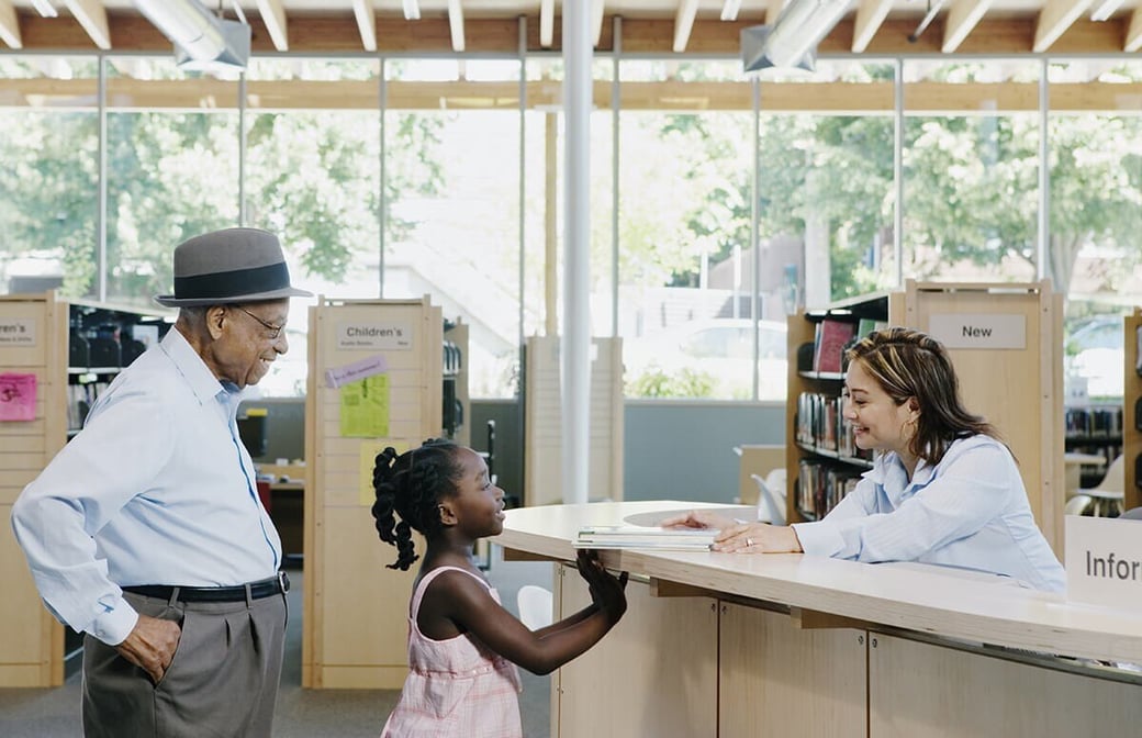 Grandfather and grandchild speaking to a librarian