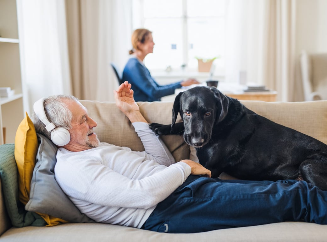 Senior man listening to audiobook with dog on couch