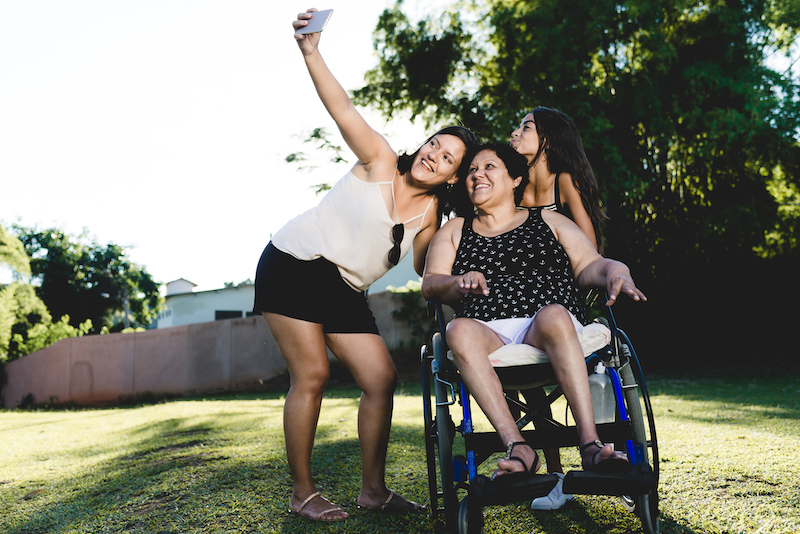 Senior woman in wheelchair taking photo with two young women