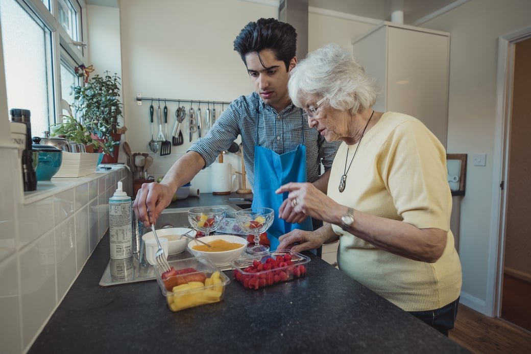 Young man helping senior woman bake in a kitchen