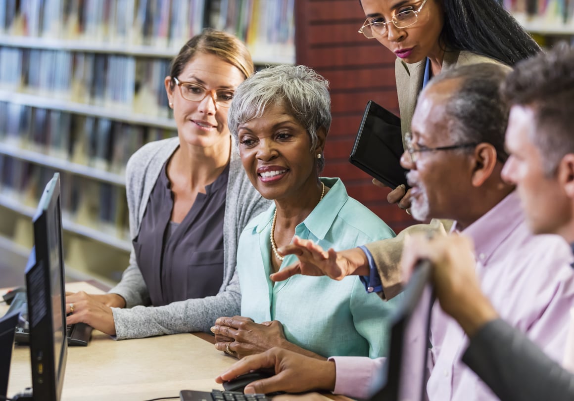 Seniors gathered around a computer, being instructed by a librarian