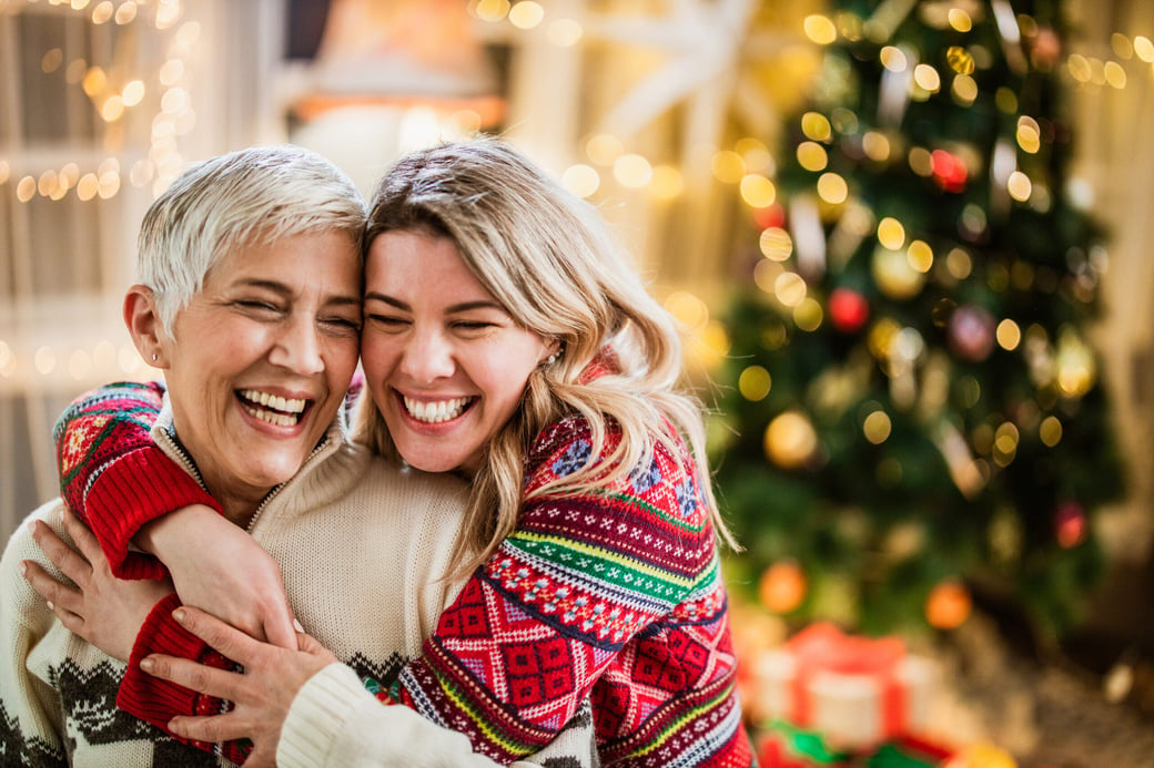 Young woman hugging senior woman in front of Christmas tree