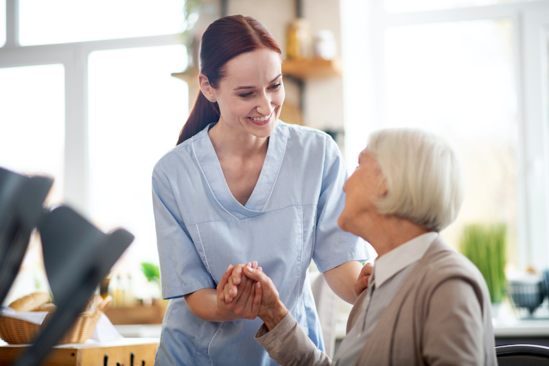 Nurse holding hand and smiling at senior woman