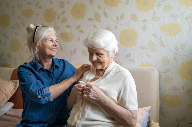 Adult woman helping senior woman put a blouse on