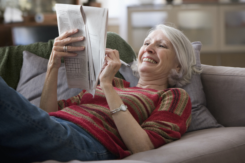 Senior woman laying on couch doing crossword puzzle