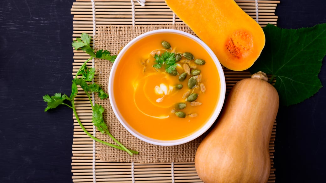 Butternut squash soup on a table next to butternut squash