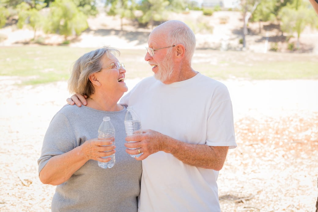 Senior man and woman smiling at each other while holding bottles of water