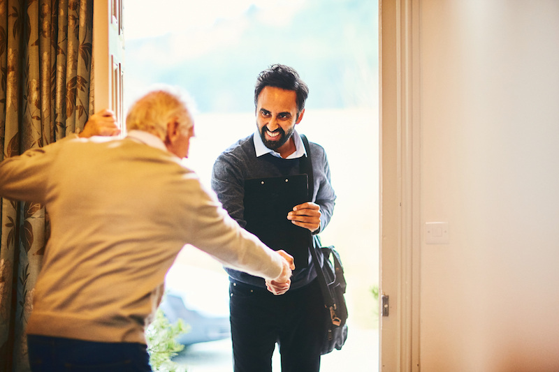 Senior man greeting younger man at his front door