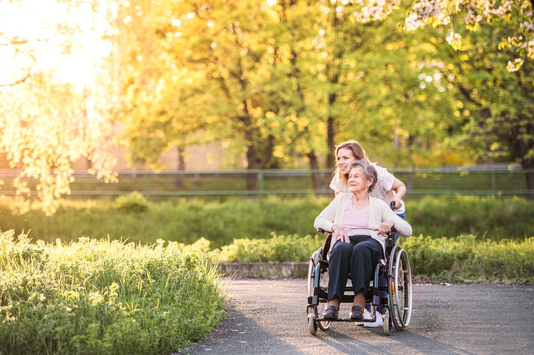 Young woman pushing senior woman in wheelchair through park