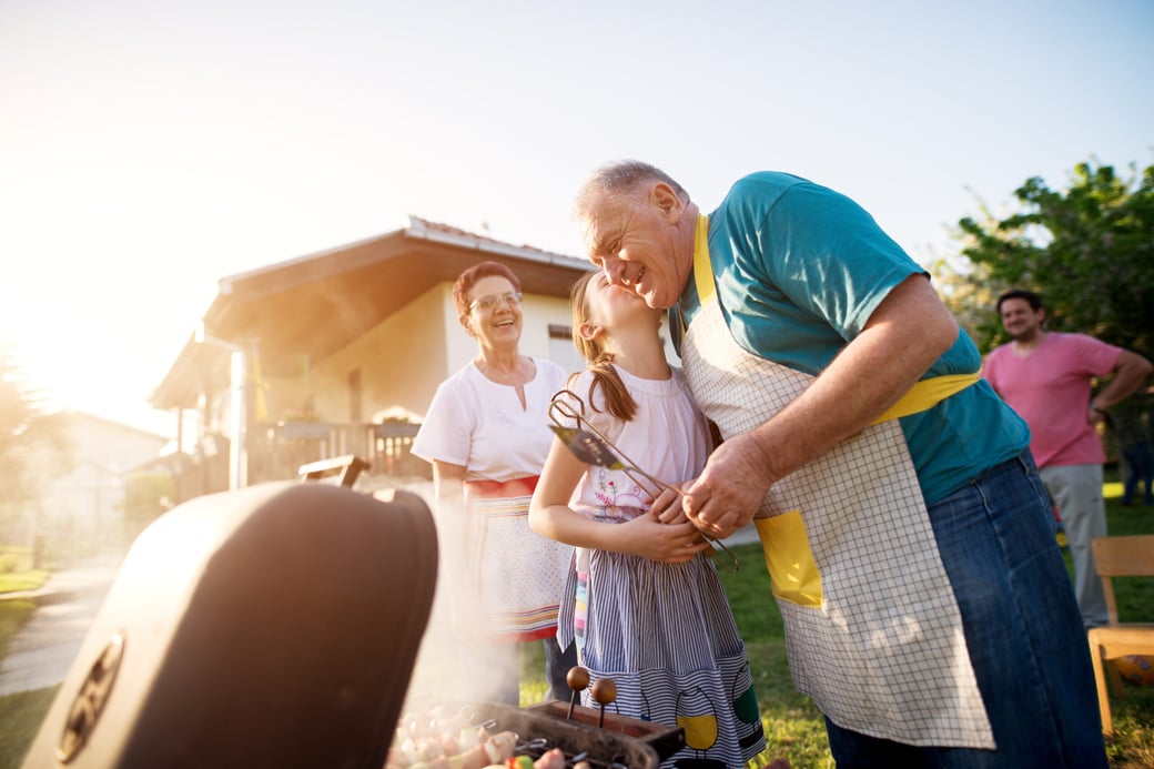 Granddaughter giving grandfather a kiss on cheek while he grills on a barbecue